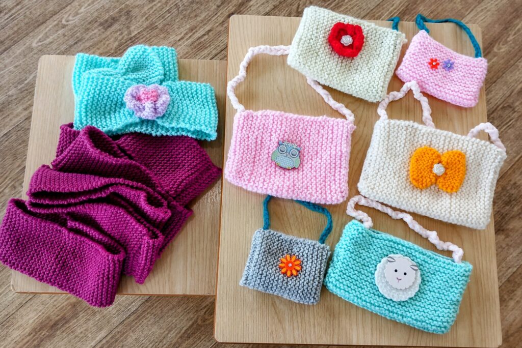 Several hand-knitted headbands and small bags with colourful patterns, crafted at Abbeyfield Lear House, create a seaside masterpiece arranged on two wooden tables.