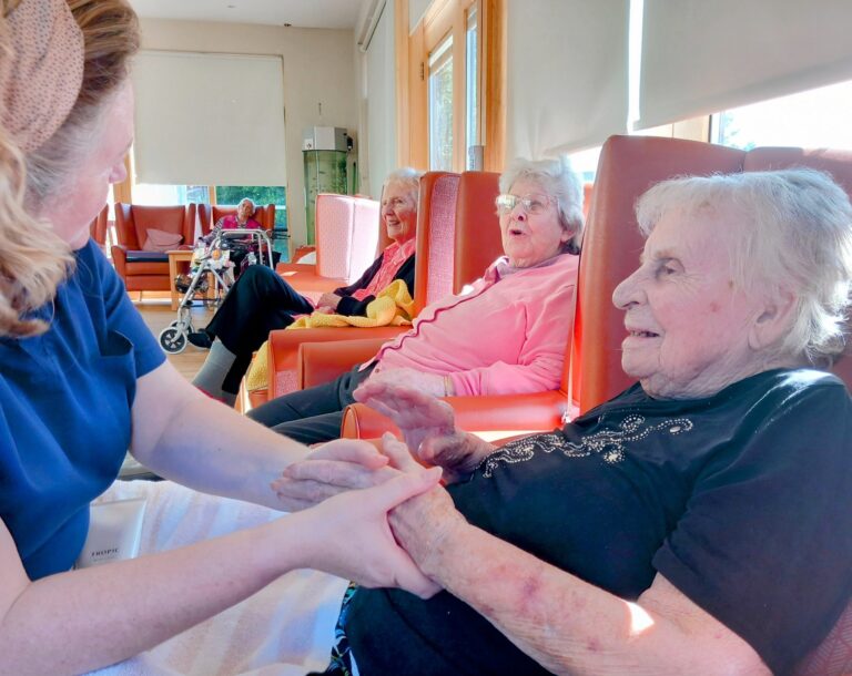 A carer holds hands with an elderly woman in a lounge at Abbeyfield, where Pamper Afternoons provide comfort and joy to residents enjoying their later years.