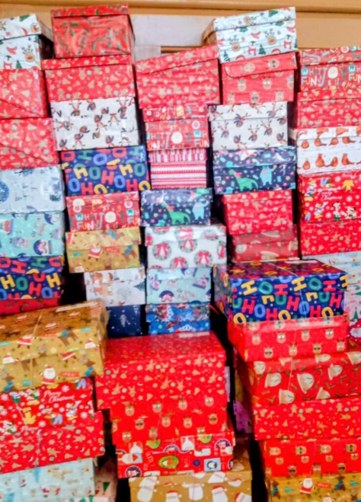 Stacks of colourful, festive Christmas shoeboxes wrapped in assorted holiday-themed papers sit closely together, spreading cheer throughout the Wirral and beyond.