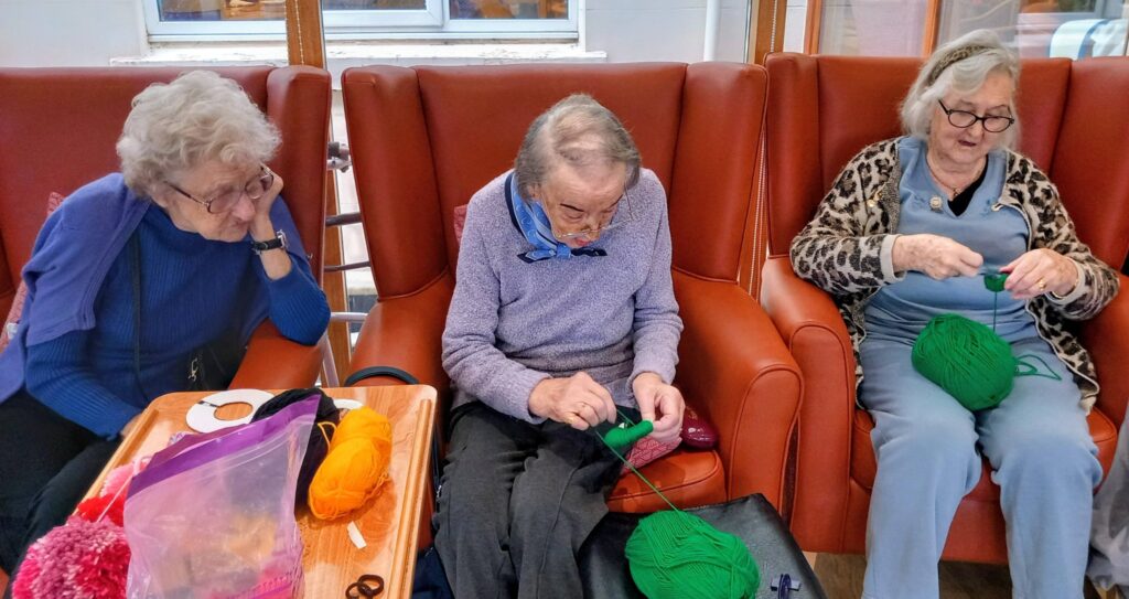A woman seated in a chair knitting, savouring a tranquil Crafternoon brimming with creativity.