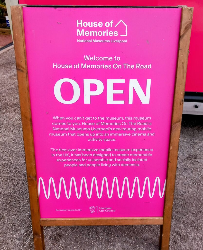 A pink sandwich board sign reads House of Memories On The Road OPEN, inviting people living with dementia and those who are socially isolated to step back in time with this unique mobile museum.