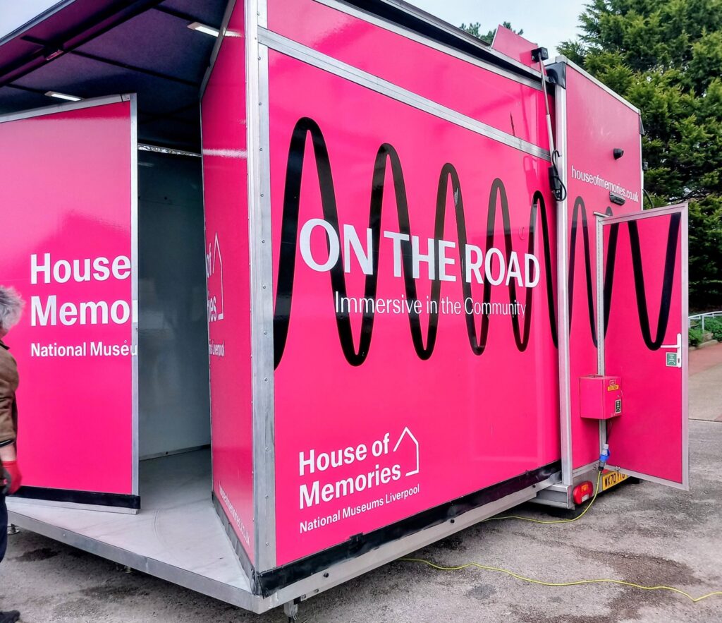 A bright pink mobile unit with "ON THE ROAD Immersive in the Community" and "House of Memories National Museums Liverpool" printed on its sides, inviting visitors to step back in time.
