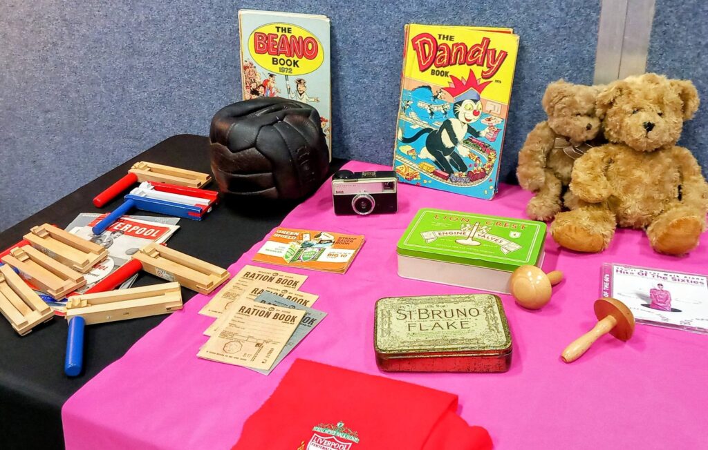 Table showcasing vintage items—including comic books, ration books, a camera and more—invites you to step back in time with the House of Memories, all set out on a pink cloth.