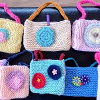 Six small, rectangular, hand-knitted bags with colourful handles and decorative circular crochet patterns are arranged on a dark surface, gently adding a touch of charm to the world.