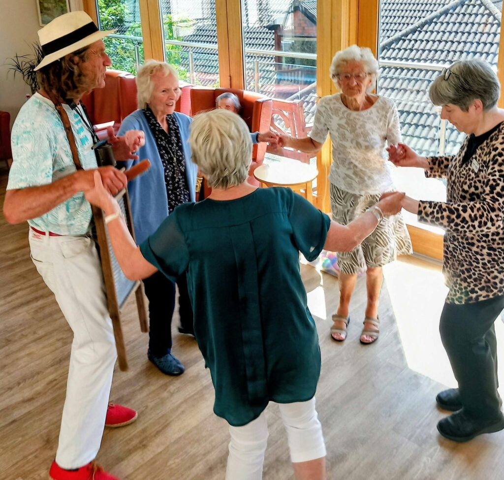 Marko and Andrew join three others, holding hands in a circle as they dance together in a sunlit room—a truly splendid afternoon brimming with joy.