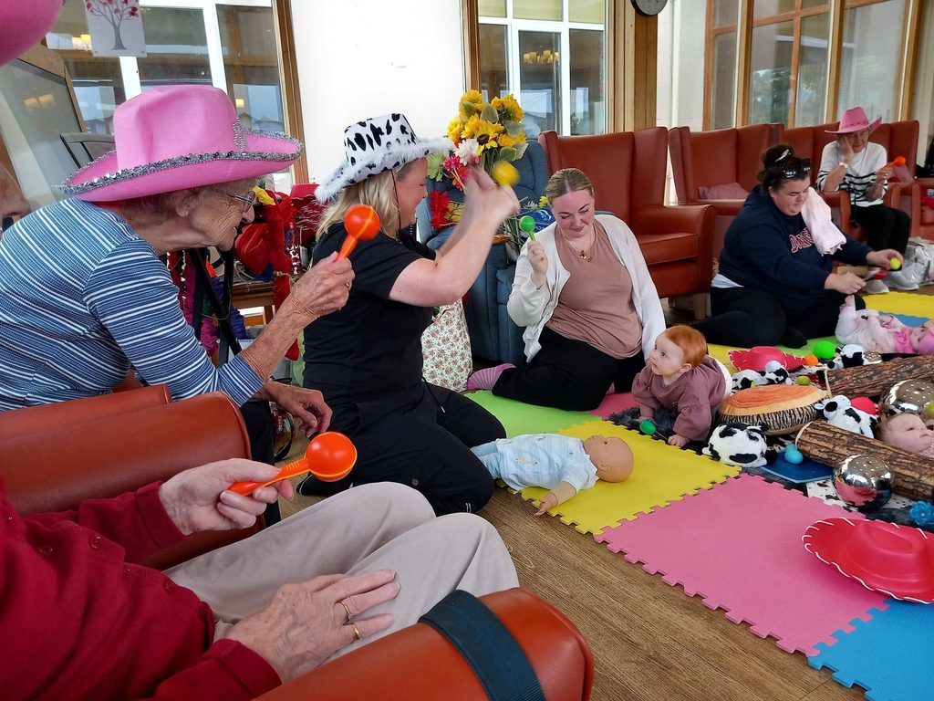 During Boogie Baby’s Wild West Week, adults and babies sit on colourful mats, shaking maracas and wearing hats, whilst soft toys and dolls are scattered across the floor.