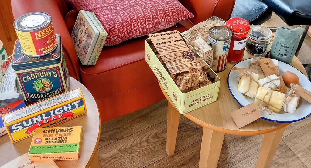 A selection of vintage food and household items arranged on a table and chair in Lear House evokes memories in a cosy room, capturing the spirit of Heswall Home Guard days.