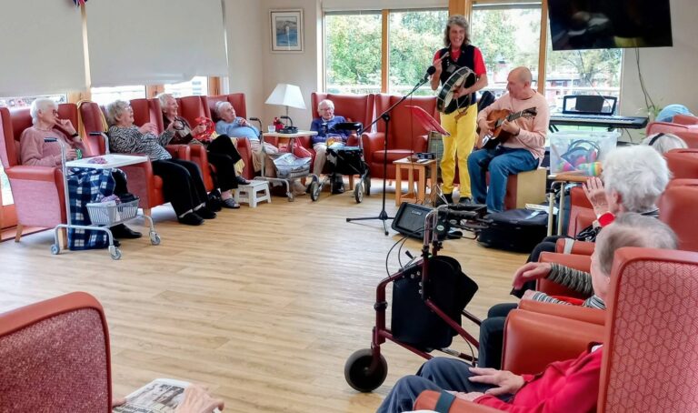 Andrew playing the bodhrán and Marko the guitarist performing for a group of elderly people seated in armchairs.