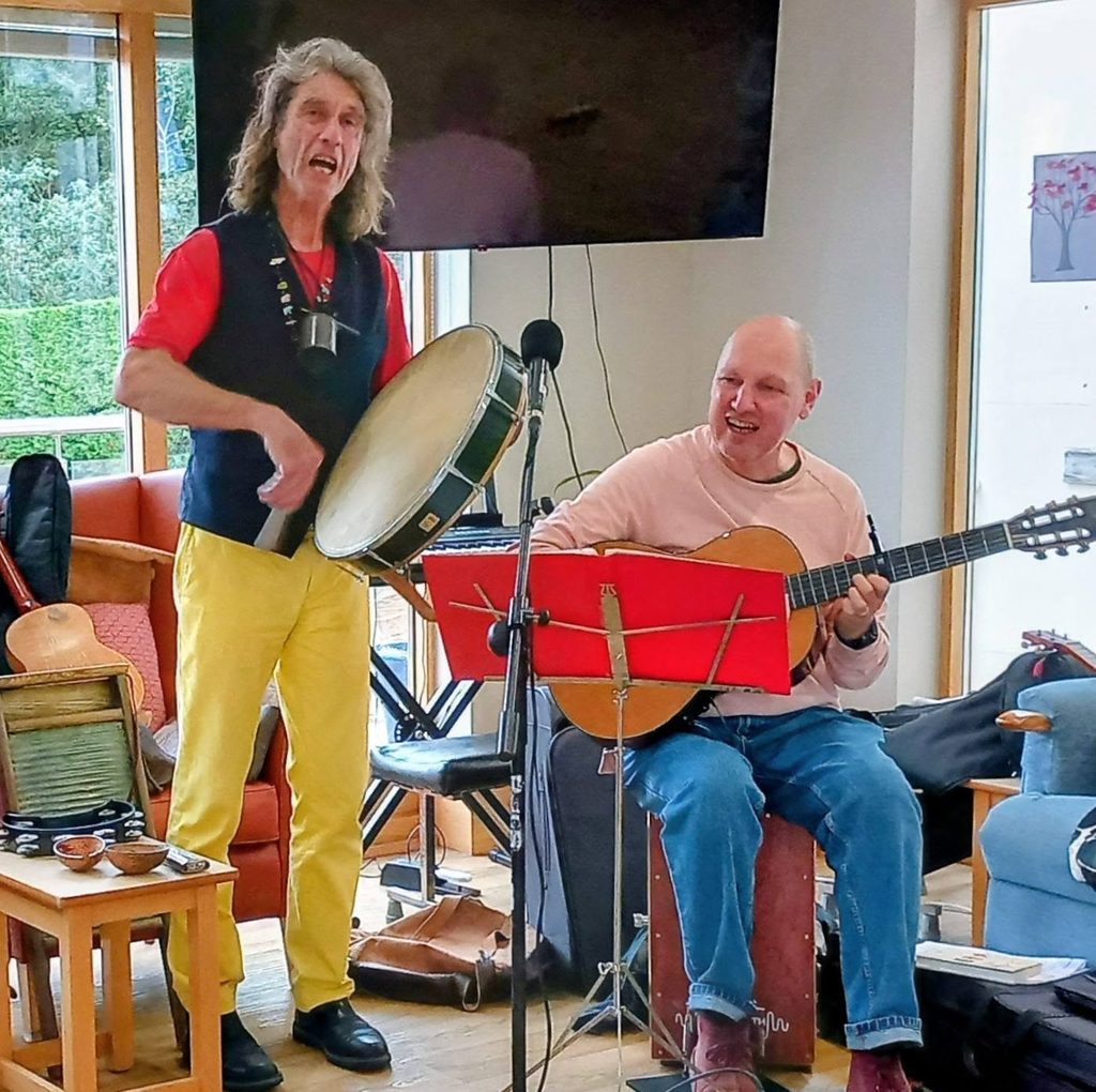 Andrew sings whilst playing a bodhrán next to Marko, who plays an acoustic guitar.