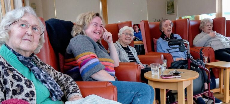 Five older adults sitting in armchairs in the Lear House communal lounge.