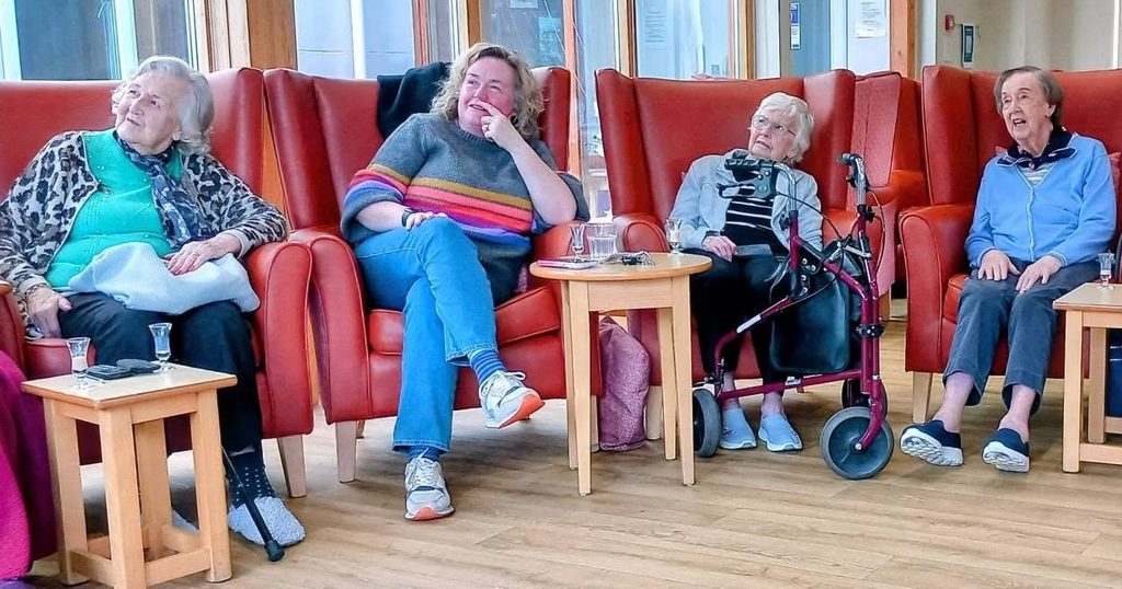 Four women, including Jess, sit in red armchairs at Lear House, looking upwards.