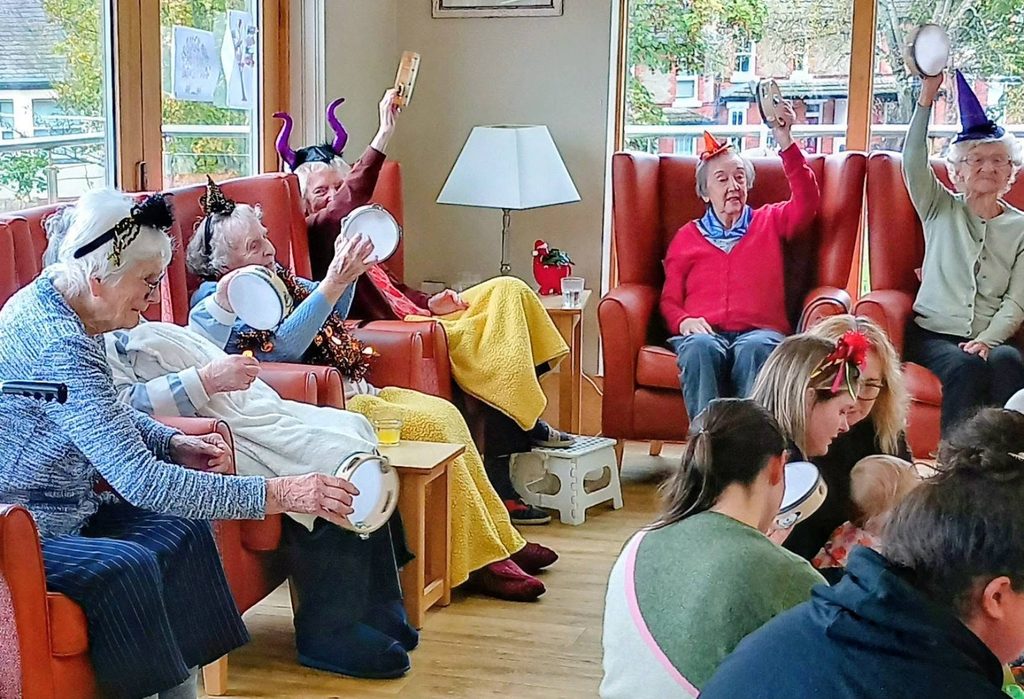 A group of older adults and younger people sitting in a circle and playing tambourines, representing connected generations.